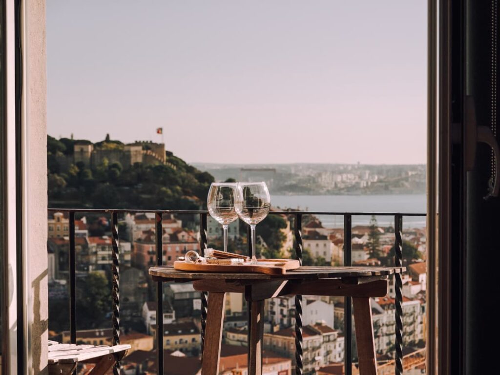 Two empty glasses of wine on a breezy balcony overlooking Lisbon's skyline and the São Jorge Castle.